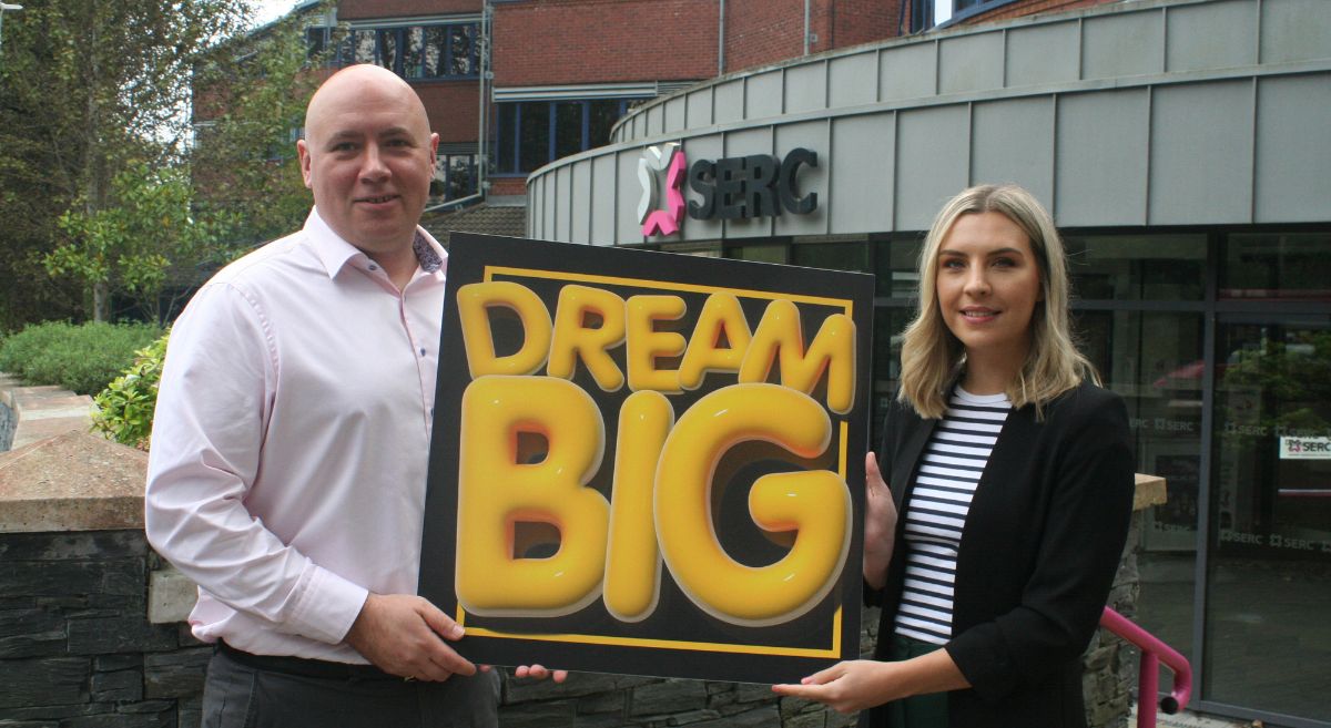 A man and a woman holding a board with the words Dream Big in yellow bubble writing with a black background pictured in front of SERC's Bangor Campus